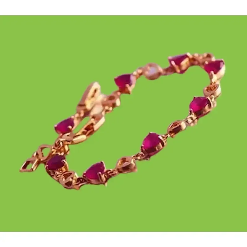 Pulsera de bisutería en oro rosa con piedra roja de imitación rubí, mostrando su brillo sobre la piel.