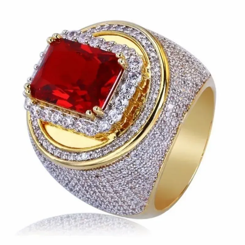 Anillo bisutería hombre chapado oro blanco con cristales rojos centrales y blancos alrededor, fondo neutro.