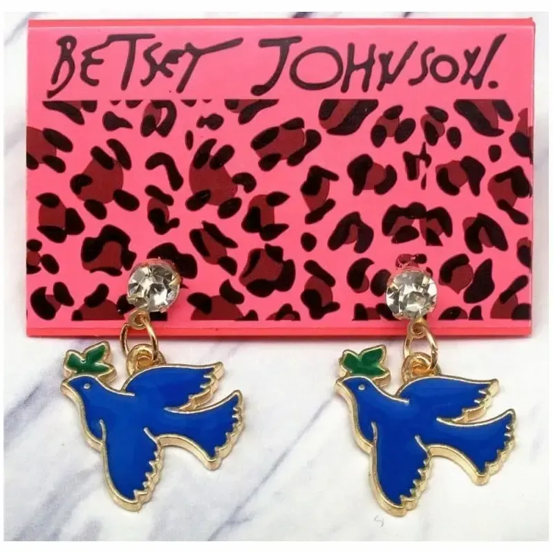 Pendientes bisutería mujer con paloma paz 2cm oro esmalte y strass, sobre fondo azul cielo.