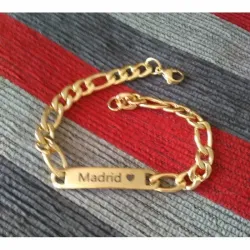 Pulsera bisutería hombre con grabado Madrid 4cm chapado oro 14K y eslabones, sobre fondo gris.