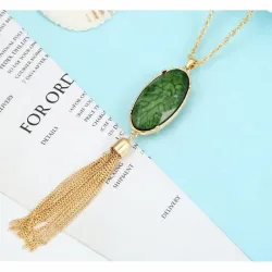 Colgante con piedra verde y borla colgando de una cadena dorada.