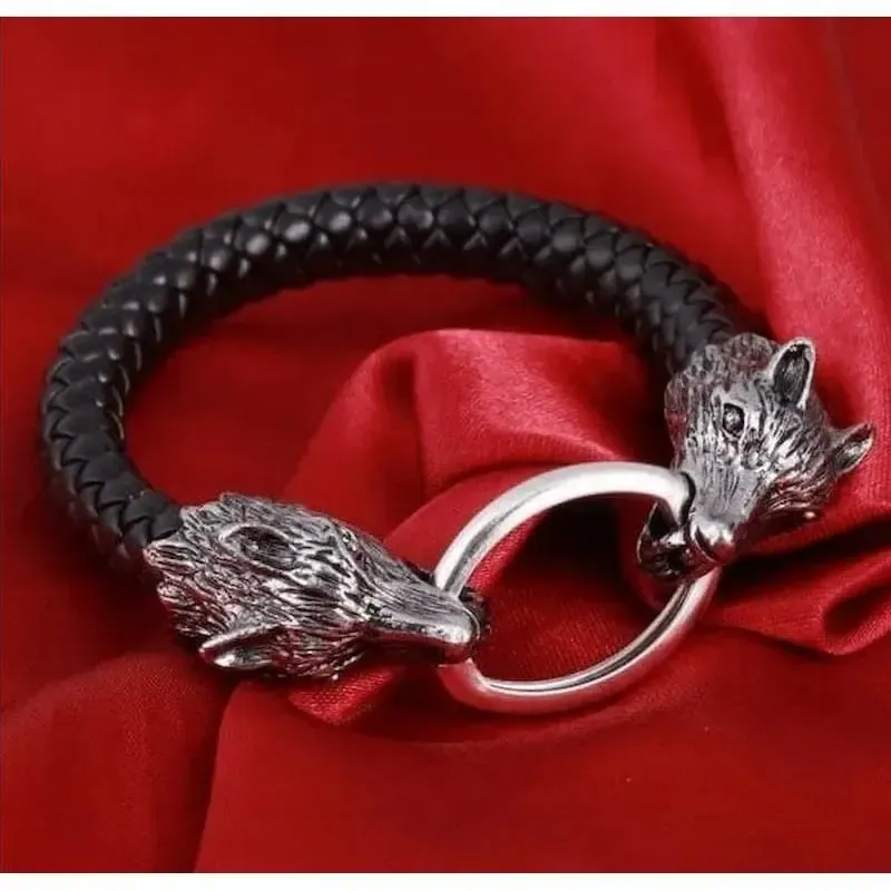 Brazalete de cuero negro con dos cabezas de lobo plateadas en los extremos.